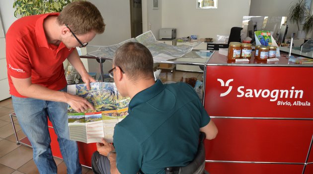 Ein junger Mann von Tourismus Savognin erklärt einem anderem Mann eine Karte. 