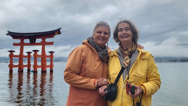 Eine Kundin mit ihrer persönliche Ferienassistentin in Japan. Im Hintergrund ein See mit bewölktem Himmel.