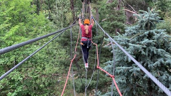 Une personne est en équilibre sur une corde en hauteur dans une forêt.
