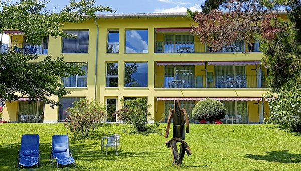 Un jardin vert avec des chaises longues devant une maison de vacances jaune. 