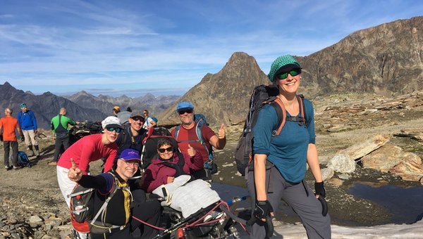 Groupe de randonneurs dans les montagnes regardant joyeusement dans l'appareil photo. Au milieu, une personne en fauteuil roulant Protrek. 